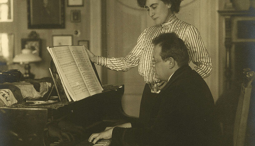 Der Komponist Reger spielt in Begleitung seiner Frau auf dem Klavier.
