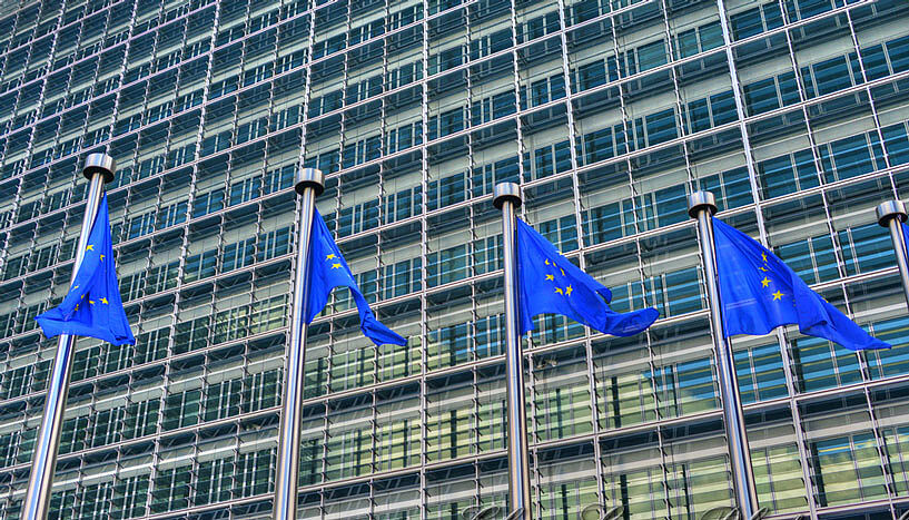 Vier Fahnen der Europäischen Union wehen vor dem gläsernen Gebäude der Europäischen Kommission im Wind.