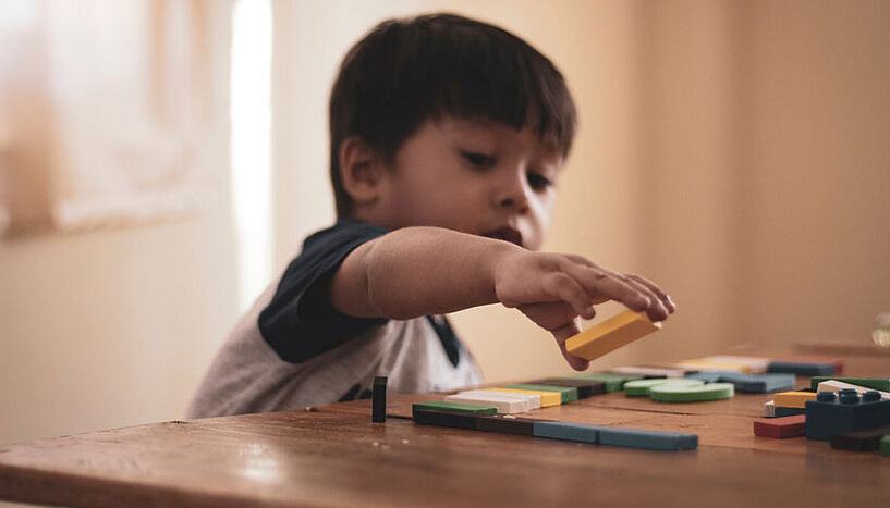 Ein Kind spielt mit Holzblöcken auf einem Tisch.