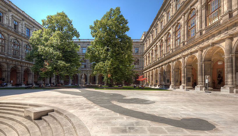 Arkadenhof des Hauptgebäudes der Universität Wien mit dem Kunstwerk "Der Muse reicht's", einem riesigen Schatten auf dem Boden, im Vordergrund.