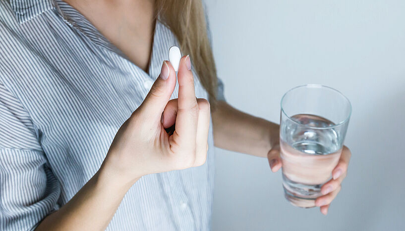 Bild einer Frau, die eine Tablette und ein Glas Wasser in der Hand häöt