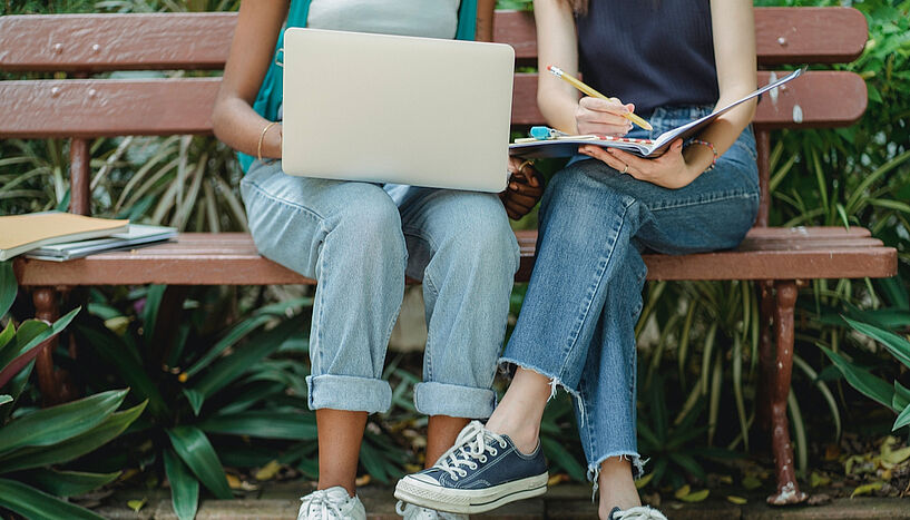 Zwei Menschen, die auf einer Parkbank sitzen und am Laptop arbeiten