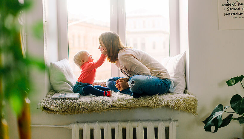 Frau und Kind sitzen auf einem Fensterbrett in der Wohnung