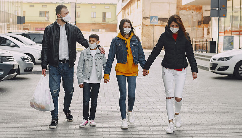 Familie trägt Mund-Nasen-Schutz und hält sich an den Händen.
