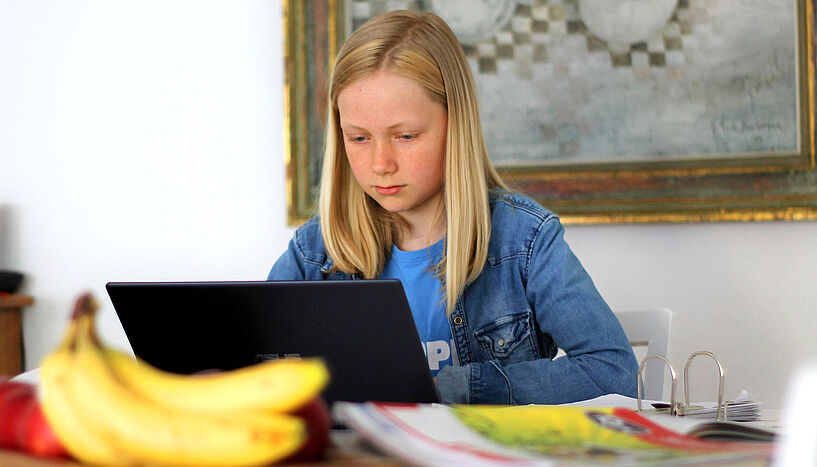 Alternativtext: Mädchen lernt zu Hause auf Schreibtisch mit Laptop