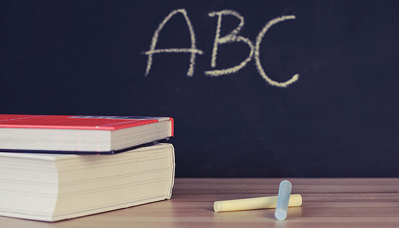 Schultafel mit ABC beschriftet, davor Bücher und Kreiden am Tisch