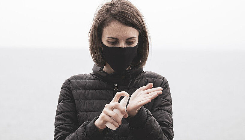 Das Bild zeigt eine Frau mit Mund-Nasen-Schutz, die sich die Hände desinfiziert.