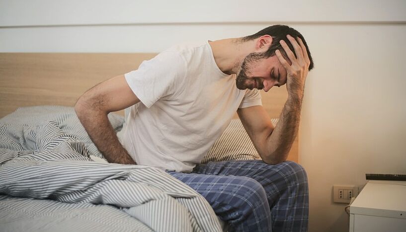 Ein Mann sitzt auf dem Bett und greift sich angestrengt an den Kopf