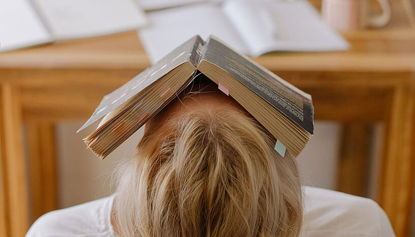 Frau lehnt sich erschöpft mit Buch am Kopf im Sessel zurück