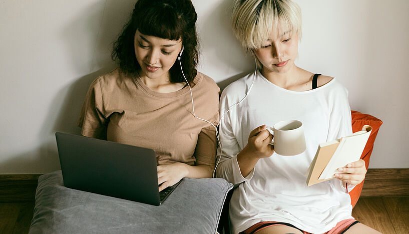Zwei lesende Frauen, eine am Laptop, die andere ein Buch