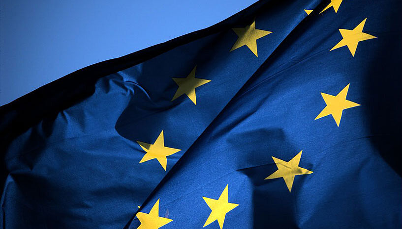 Eine Flagge der Europäischen Union flackert im Wind. Die Sonne leuchtet durch den Stoff.