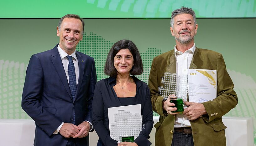 Preisträger Gerhard Weber (rechts) steht mit der Auszeichnung in der Hand vor einem grün-weißen Hintergrund. Auch auf dem Foto: Landesrat Jochen Danninger (links) und Sonia Vallet von der Med Uni (mitte)