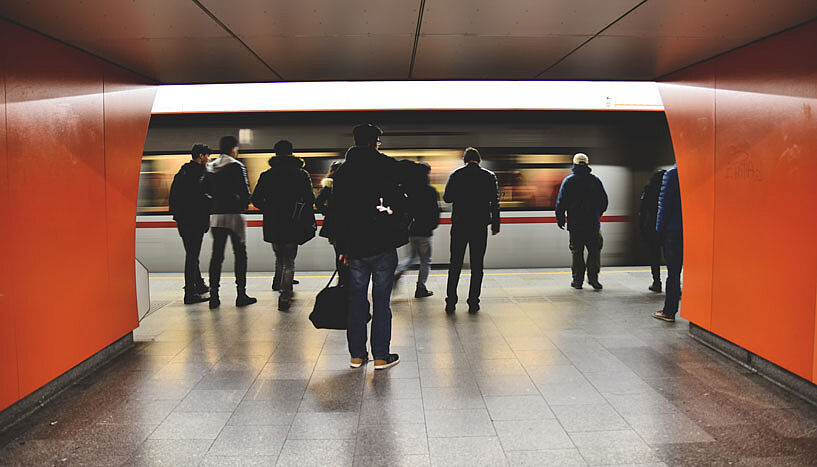 Eine Gruppe von Menschen steht in einer Ubahnstation, während ein Zug einfährt.