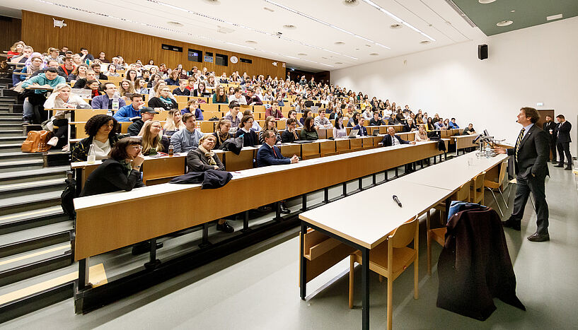 Trevor Traina, US-Botschafter in Wien, hält Vortrag vor einem vollen Hörsaal an der Universität Wien.
