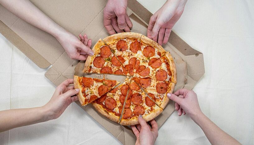 Picture of several hands reaching for a pizza.