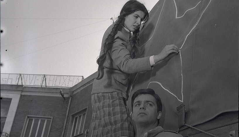 Zwei junge Menschen stehen vor einer Hauswand, eine malt einen Stern mit Kreide auf die Hauswand. 