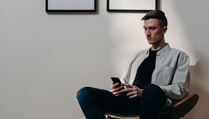 Man sits on a chair and looks into his phone