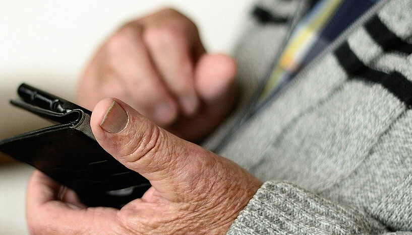 Hände einer älteren Person, die ein Smartphone hält