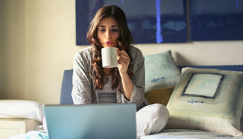 Bild einer Frau, die auf einem Bett sitzt und etwas am Laptop macht